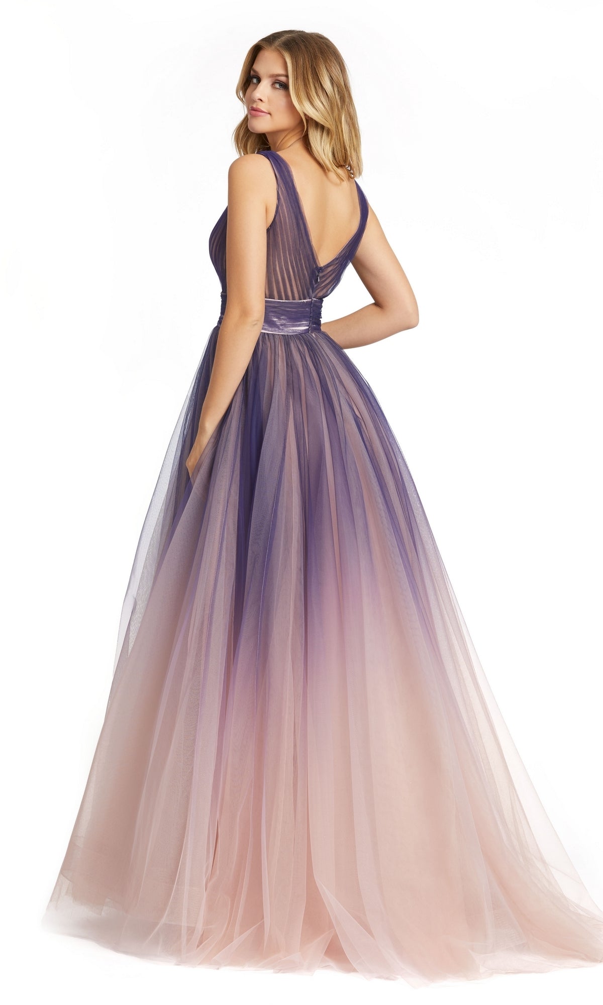 A woman poses with her back slightly turned, wearing the Indigo Ombre Prom Ball Gown (Mac Duggal 20221), featuring a sleeveless fitted bodice and a floor-length gradient tulle skirt in shades of purple and blush.